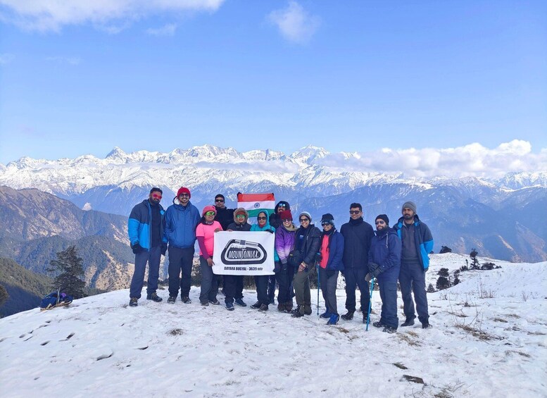 A group of people standing on a snowy mountain peak with a banner, snow-covered mountains in the background. 2