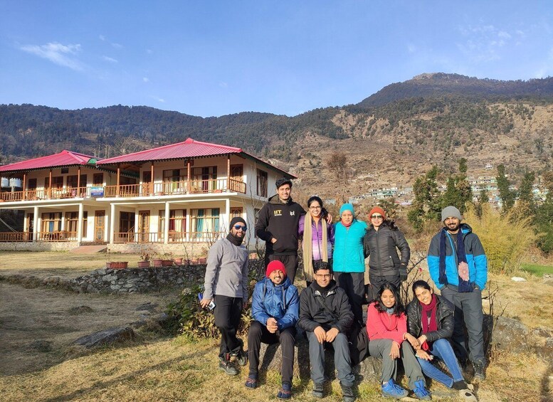 A group of people posing in front of a building with a red roof, set against a mountainous backdrop. 3