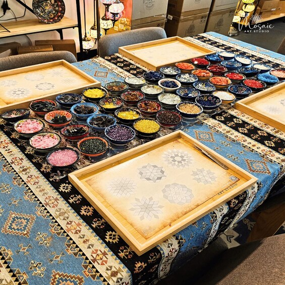 A table with trays of colorful beads and a patterned tablecloth. 4