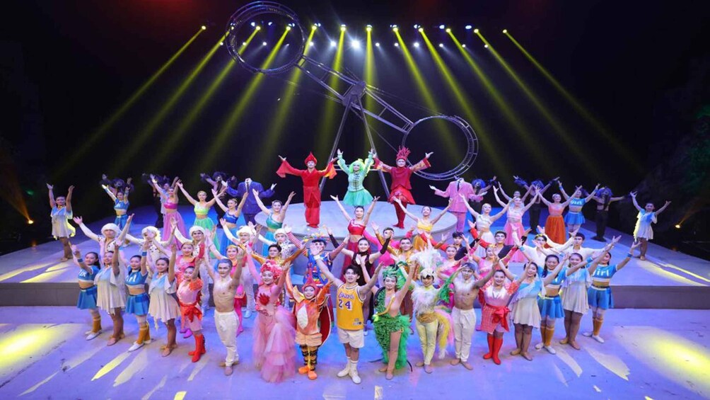 A group of performers on a stage with colorful costumes and a circus ring in the background. 2