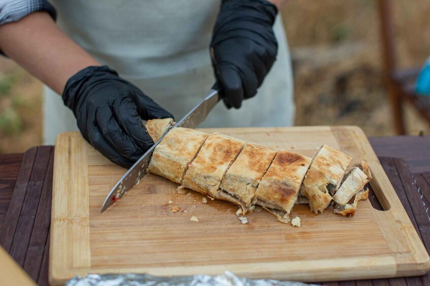 A person slicing a large, rectangular pastry on a wooden cutting board. 5
