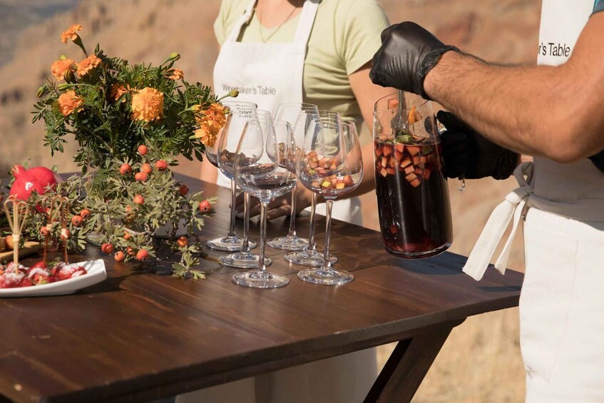 A person pouring a drink into wine glasses on a table with flowers and a pomegranate. 3