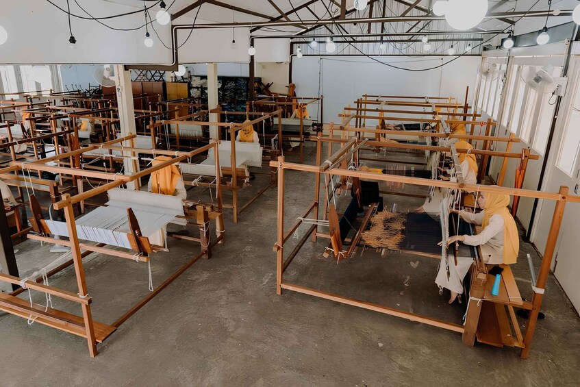A workshop with multiple weaving looms and workers. 1