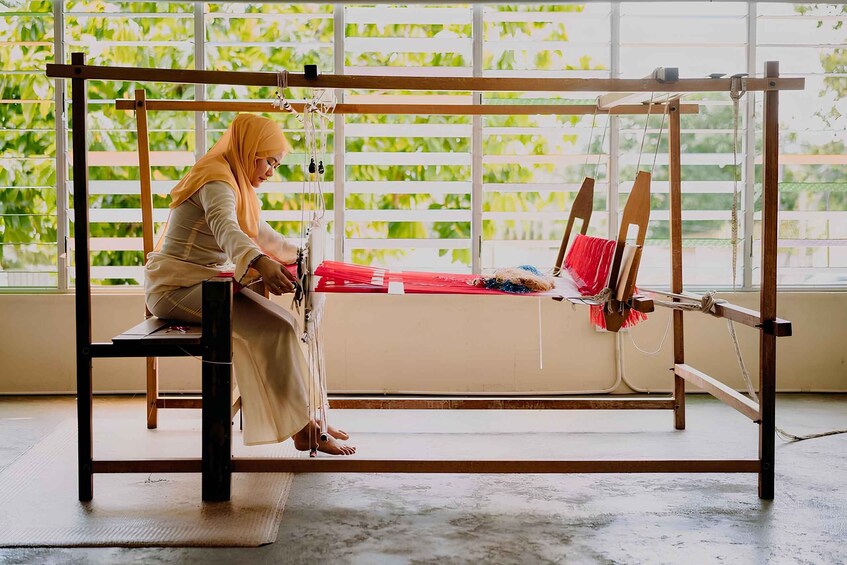 A person weaving at a wooden loom with a window in the background. 4