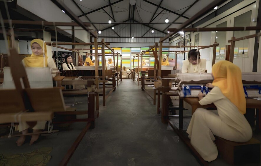 A workshop with people working at wooden tables, some wearing headscarves. 3