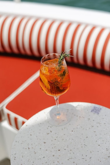 A cocktail glass with a garnish on a white table with a red and white striped cushion in the background. 4