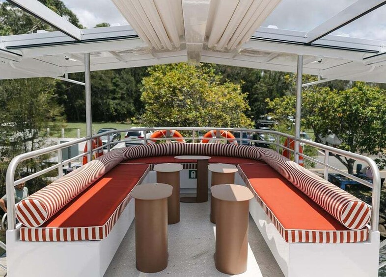 A covered outdoor seating area with striped cushions and round tables. 3