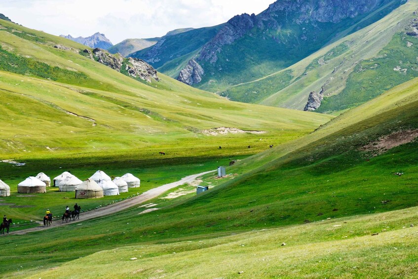 A mountainous landscape with green valleys, yurts, and a dirt road. 4