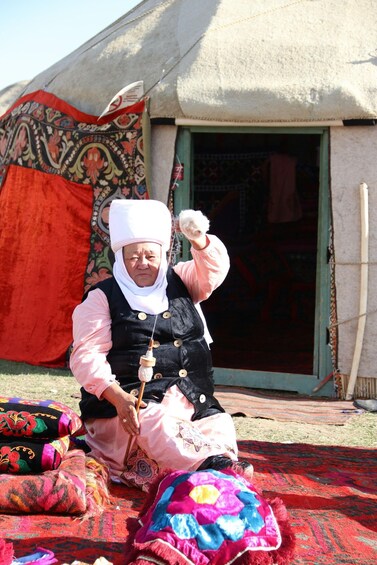 A person sitting on a colorful rug in front of a traditional yurt with a patterned blanket and a door. 2