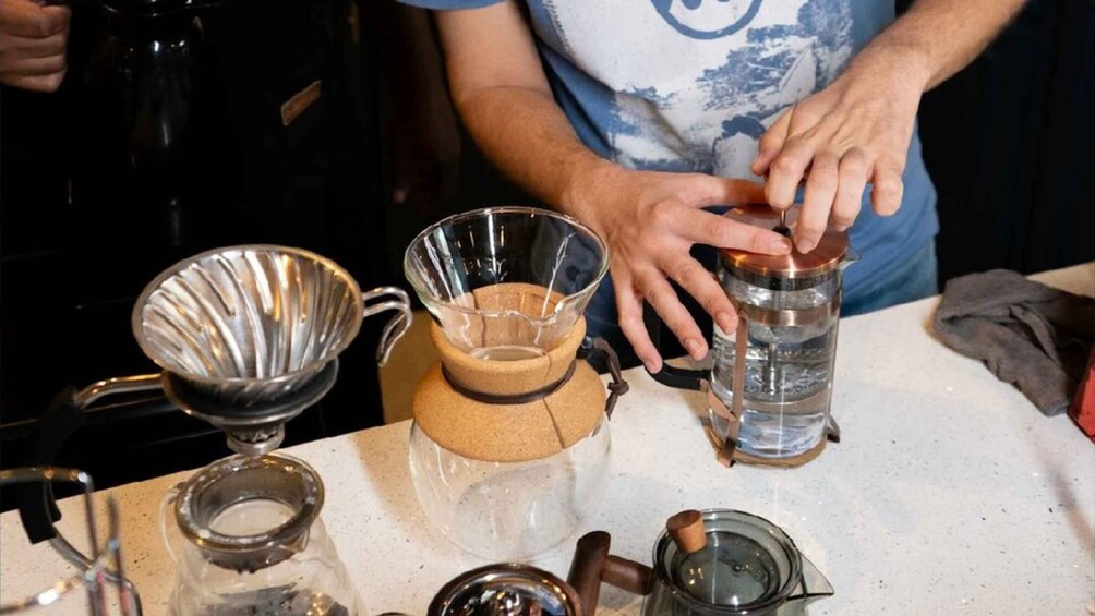 A person preparing a drink with a coffee press, a glass, and a kettle on a kitchen counter. 4