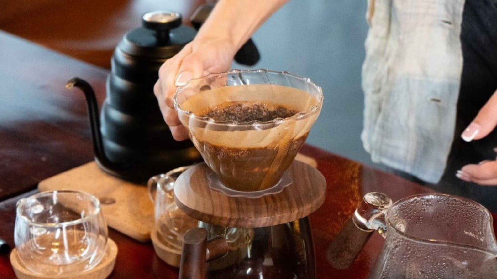 A person pouring a dark liquid from a glass into a wooden container. 3