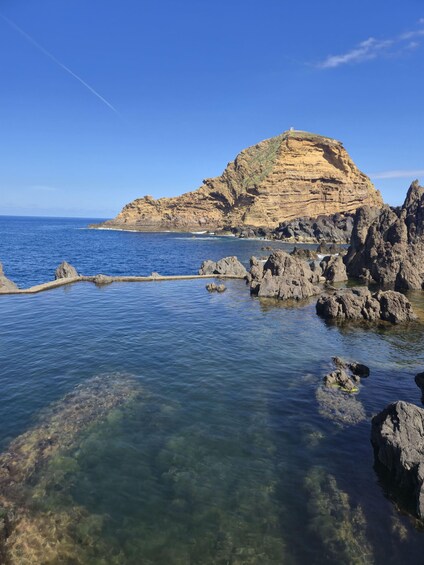A coastal landscape with clear blue waters, rocky formations, and a prominent hill with a lighthouse. 2