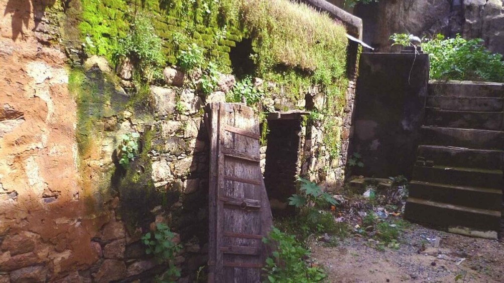A rustic stone building with moss-covered walls, a wooden door, and a metal gate. 2