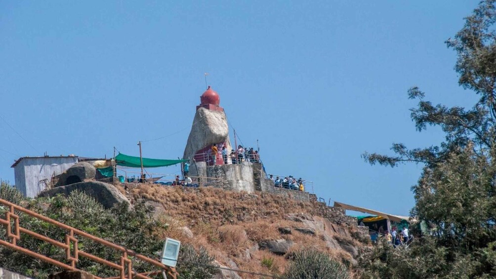 A large rock formation with a red top, surrounded by a small crowd of people. 4