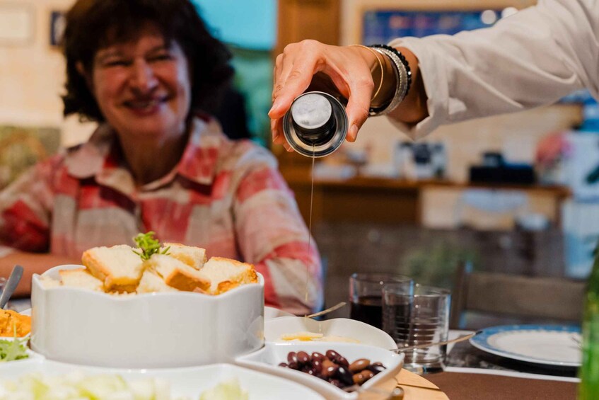 A person pouring a liquid from a small container onto a dish with bread. 1