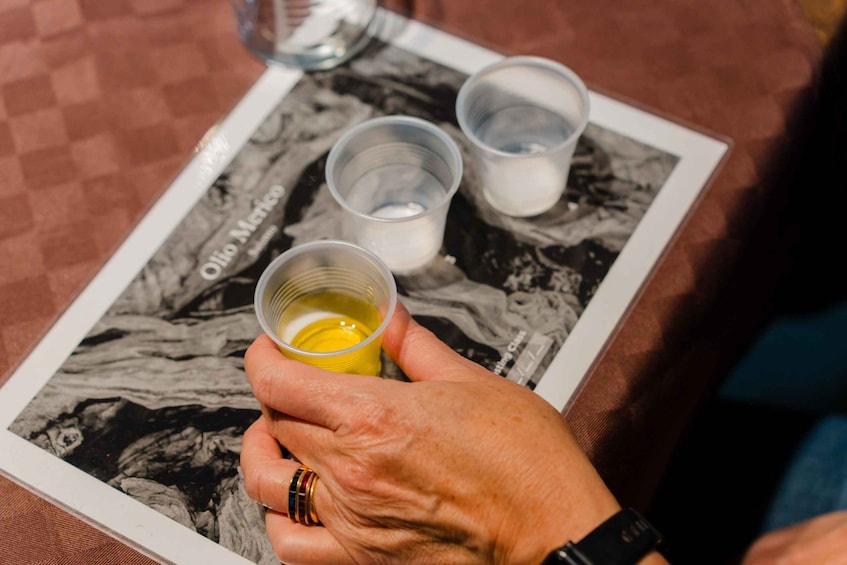 A hand holding a cup with a yellow liquid, possibly juice or oil, over a magazine or brochure. 3