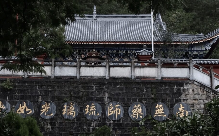 A traditional Chinese building with a tiled roof and a stone wall with inscriptions. 4