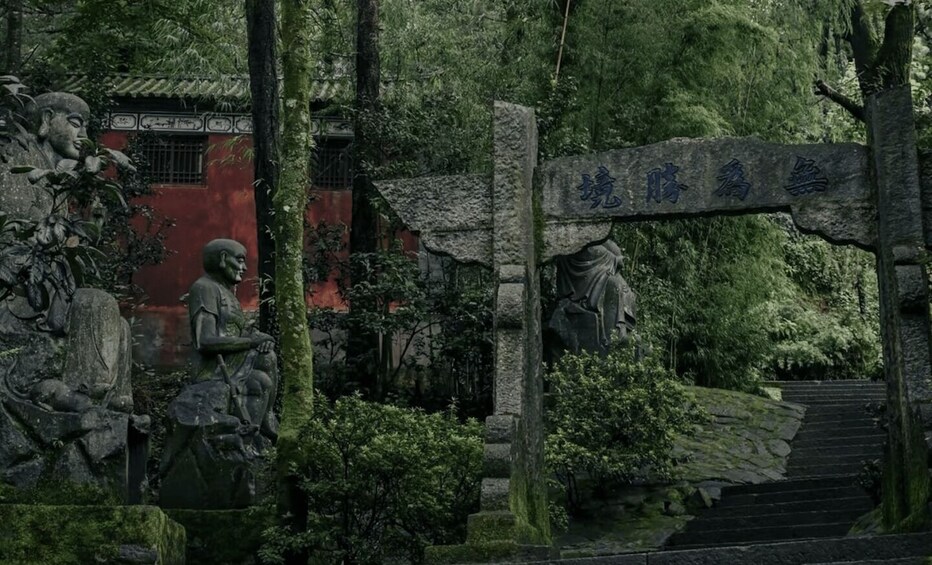 A traditional Chinese gate with stone carvings, surrounded by lush greenery and a red building in the background. 3