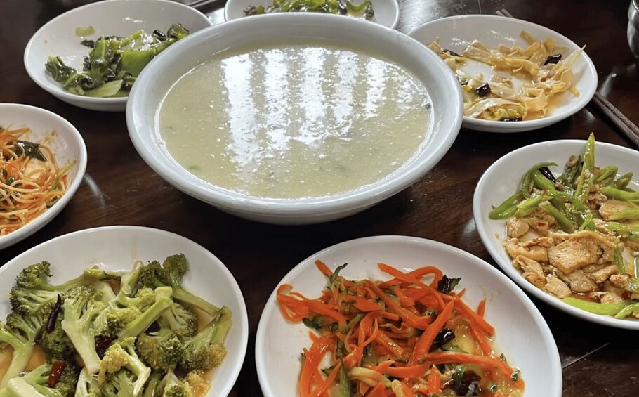 A variety of dishes including a large bowl of soup, several plates of stir-fried vegetables, and a dish with sliced carrots and green beans. 5