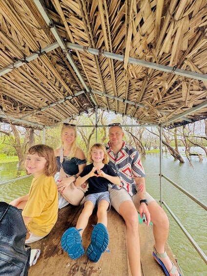 A group of people on a boat with a thatched roof, surrounded by water and trees. 5