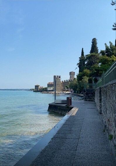A waterfront promenade with a stone wall, a clear blue sky, and historic buildings in the background. 4