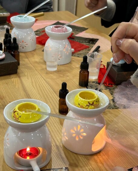 A table with several small white ceramic containers, some with liquids and others with solid substances, and a lit candle. 3