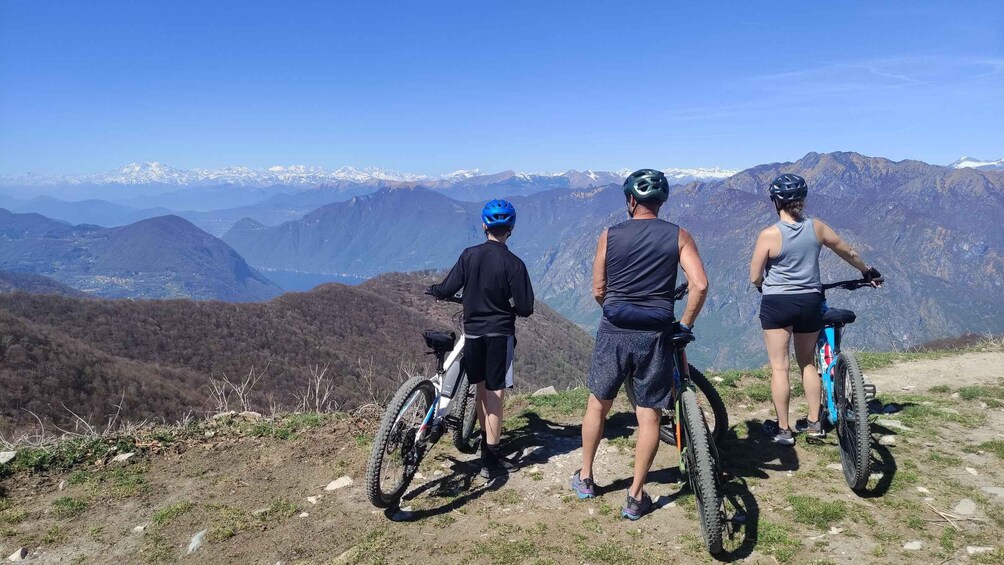 Three cyclists on a mountain trail with a view of snow-capped mountains in the background. 1