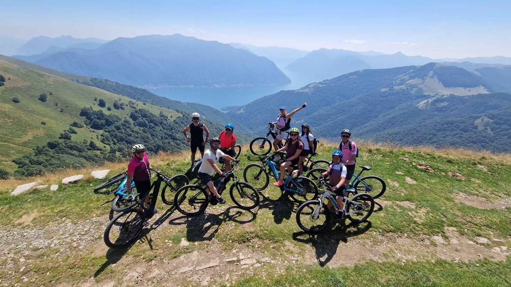 A group of cyclists on a mountain trail with a scenic view of distant mountains and a lake. 4
