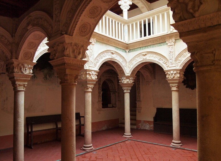 An interior courtyard with ornate arches and columns, a wooden bench, and a red brick floor. 4