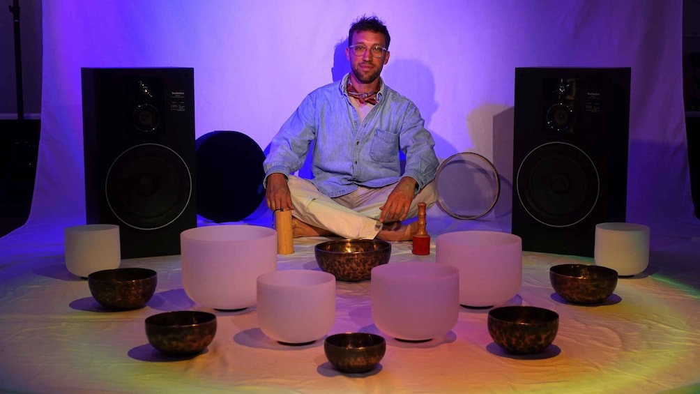 A person seated on a chair surrounded by bowls and speakers. 3