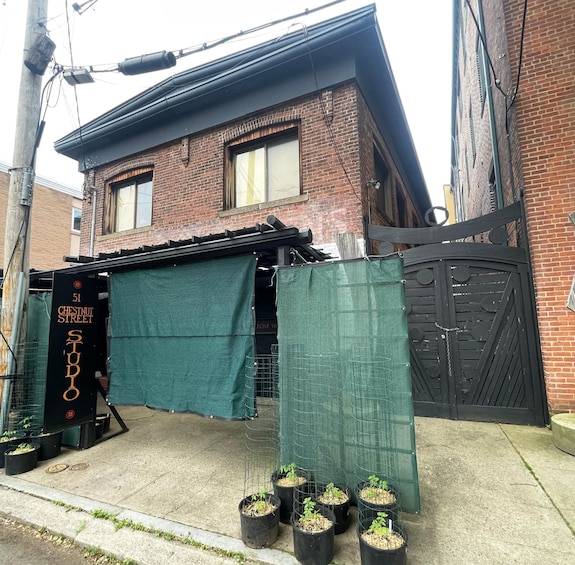 A brick building with a green tarp covering part of the entrance, a black gate, and several potted plants on the sidewalk. 4