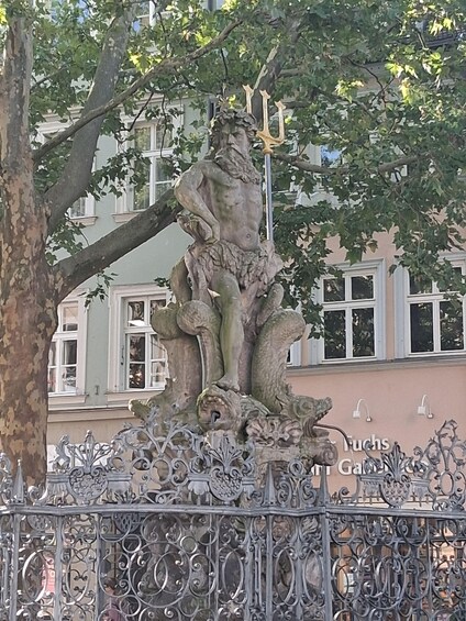 A statue of a man with a snake, set in a metal fence with ornate designs, in an urban setting with buildings in the background. 2