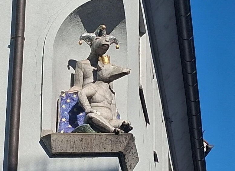 A sculpture of a figure with a crown and a jester hat, seated on a pedestal. 5
