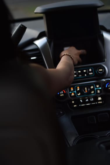 A person's hand on a car's central console with illuminated buttons and a display. 2