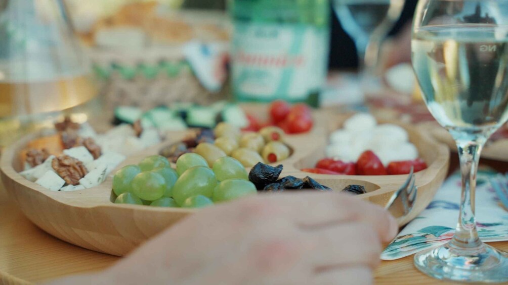 A wooden board with various fruits and nuts, a glass of white wine, and a blurred background with a bottle. 5