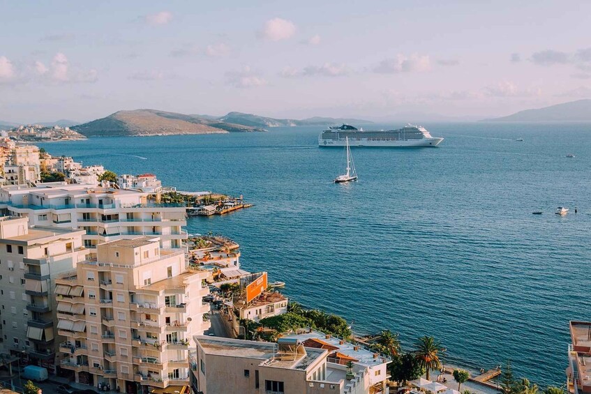 A cruise ship in the ocean, a sailboat, and coastal buildings. 1