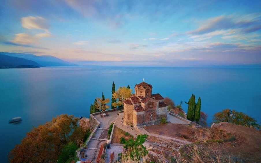 A historic church on a hill overlooking a calm lake with a clear sky. 3