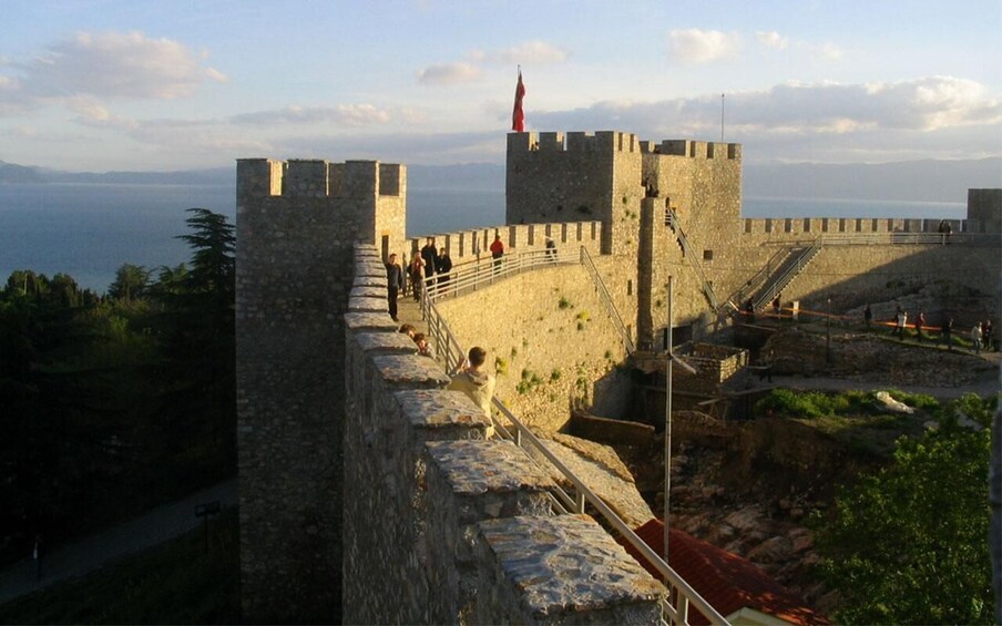 A stone fortress with a flag on top, a staircase leading up to the entrance, and a view of the sea in the background. 4