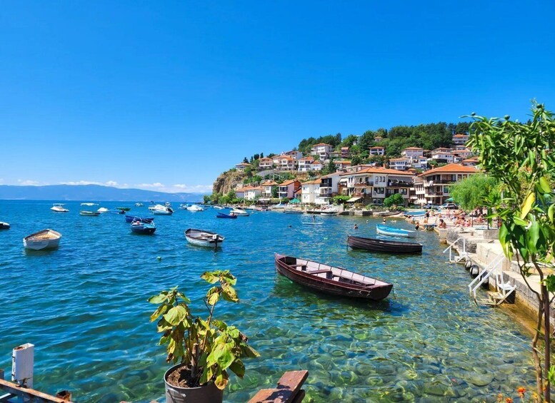 A coastal town with boats on the water, clear shallow areas, and houses on a hillside. 1
