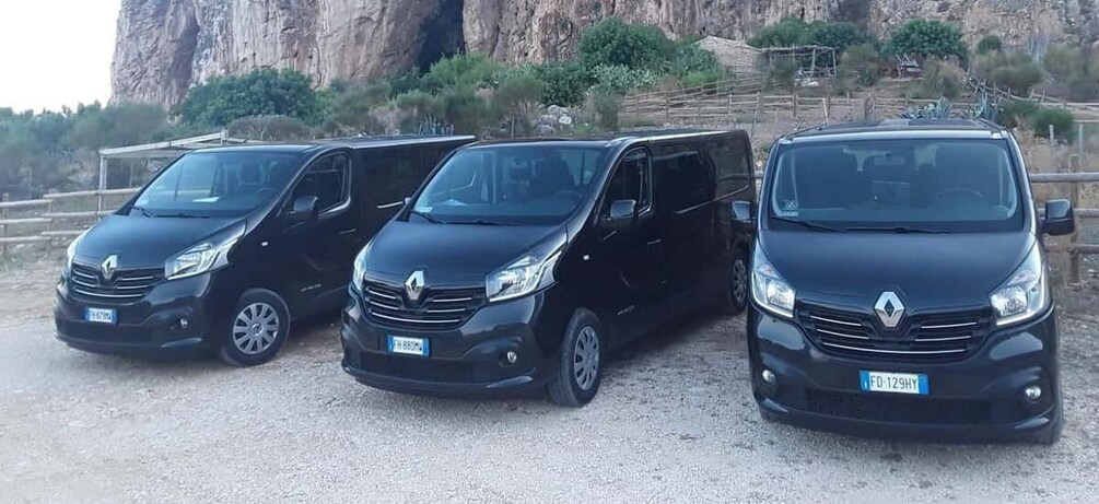 Three black Renault vans parked on a gravel surface with a rocky cliff and sparse vegetation in the background. 3