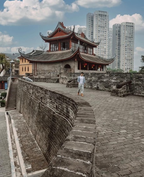 A traditional Chinese building with a curved roof, a stone wall, and a staircase leading up to it. 1