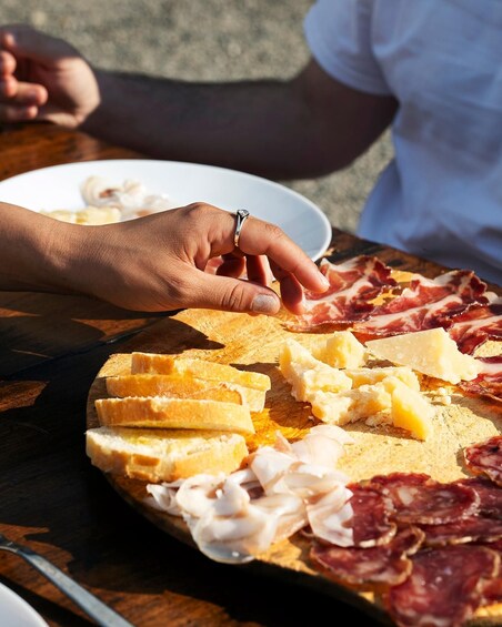 A wooden board with sliced bread, cheese, and cured meats. 1