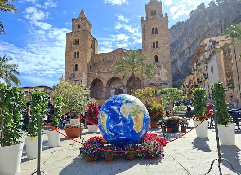 A large globe surrounded by potted plants and flowers, with a historic building in the background. 4