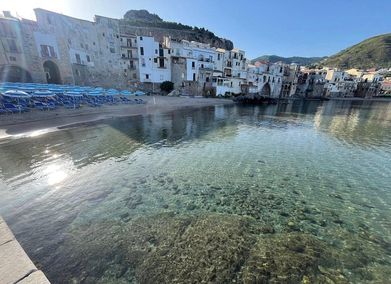 A coastal town with clear waters, white buildings, and blue beach umbrellas. 5