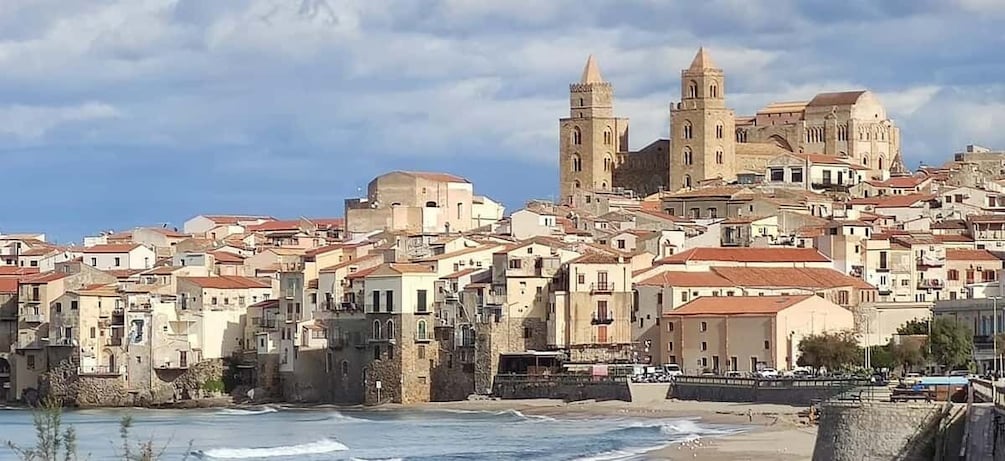 A coastal town with historic buildings, a prominent church with two towers, and a beach in the foreground. 2