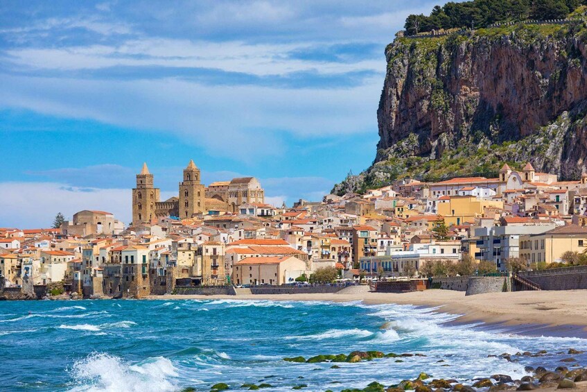 A coastal town with historic buildings, a prominent church with two towers, and a steep cliff. 1