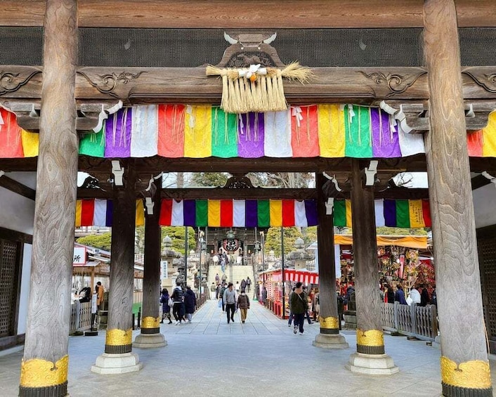 A traditional wooden structure with colorful flags, a central decorative element, and a pathway leading to a shrine. 5