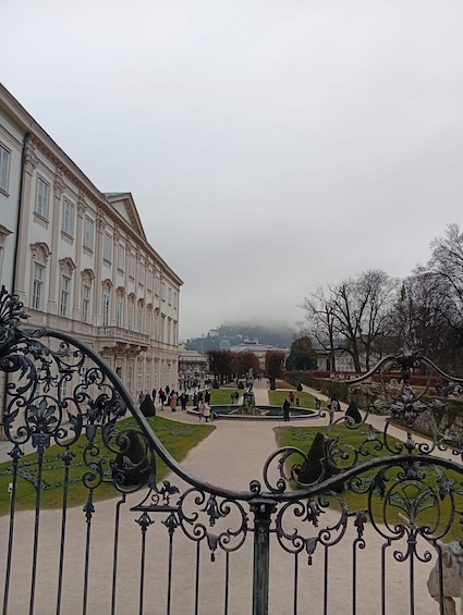 A classical building with ornate ironwork, a central fountain, and a formal garden. 3