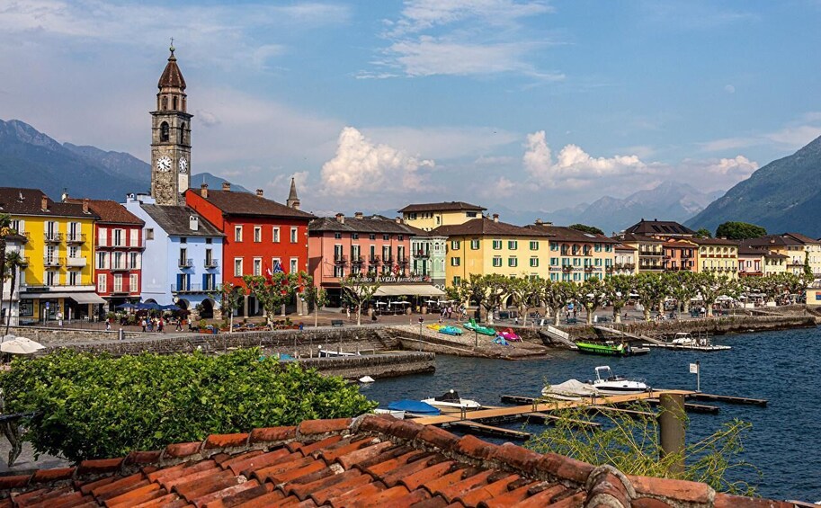 A colorful waterfront town with a prominent clock tower, a variety of buildings, and boats docked at the marina. 1