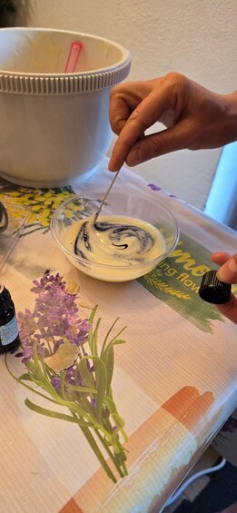 A person stirring a yellow liquid in a glass bowl, with a floral tablecloth and a jar of black liquid nearby. 1